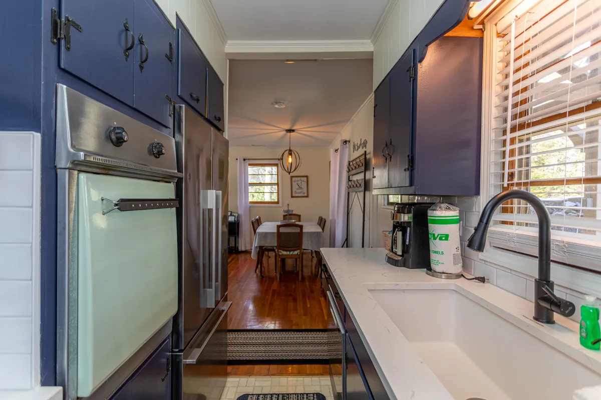 A bright, modern kitchen featuring stainless steel appliances, a kitchen sink, and a dining table set near a window that lets in abundant natural light. The scene suggests an open, sociable space ideal for cooking and entertaining.