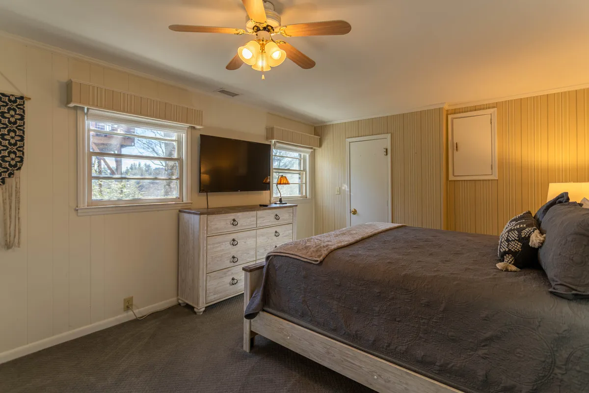 A bedroom featuring a cozy bed, dresser, television, and windows that allow sunlight to stream in. This creates an inviting atmosphere for both relaxation and entertainment, reflecting personal touches like private TVs mentioned in the section.