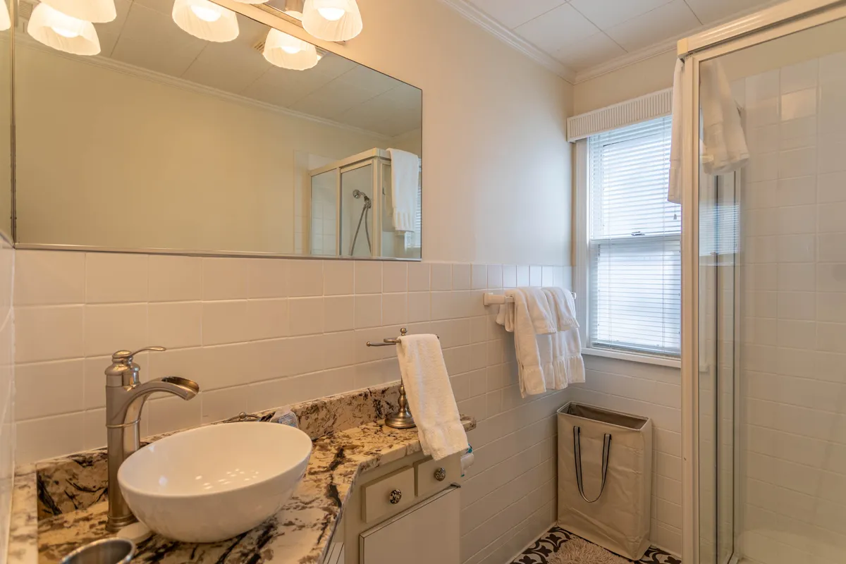 A modern bathroom with an oval sink, granite countertop, well-lit mirror, and an inviting shower area. The calming décor and quality finishes underscore the bathroom amenities available for relaxation and privacy.