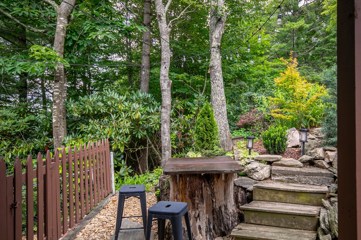 A wooden bar table with stool seating is set against natural landscaping and stone steps, creating a relaxed and inviting space for outdoor gatherings. The area is surrounded by greenery and offers a sense of seclusion and serenity, ideal for enjoying morning coffee or evening cocktails.
