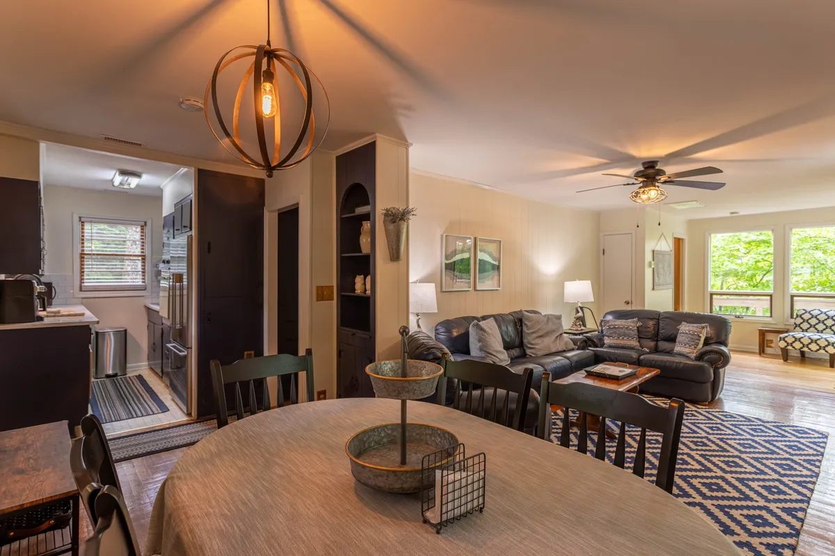 A comfortable living area with a sofa and a large window bathing the room in natural light, adjacent to a dining table set for a meal. Decorative touches and a casual arrangement invite relaxation and lively gatherings.