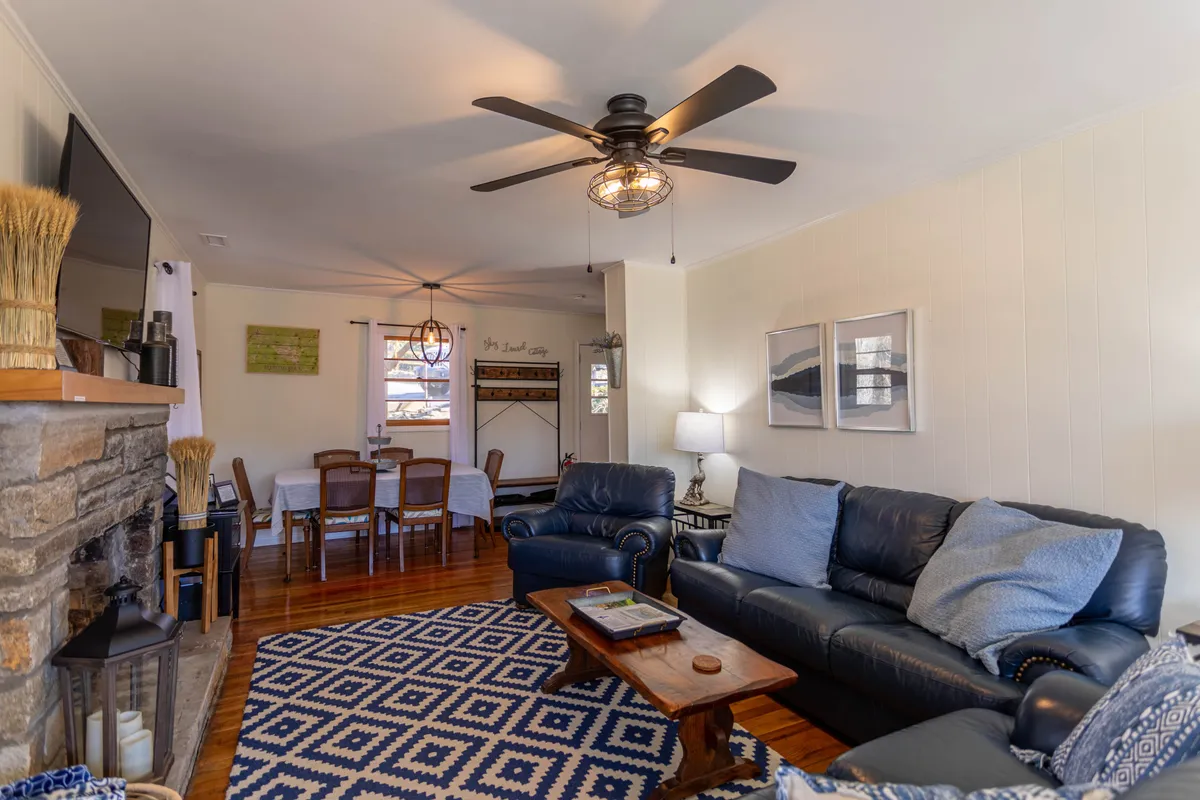 This image captures an open-concept living space featuring leather sofas, a wooden coffee table, a prominent stone fireplace, and a visible dining area in the background. The overall atmosphere is warm and inviting, perfect for family relaxation, socializing, and shared meals.