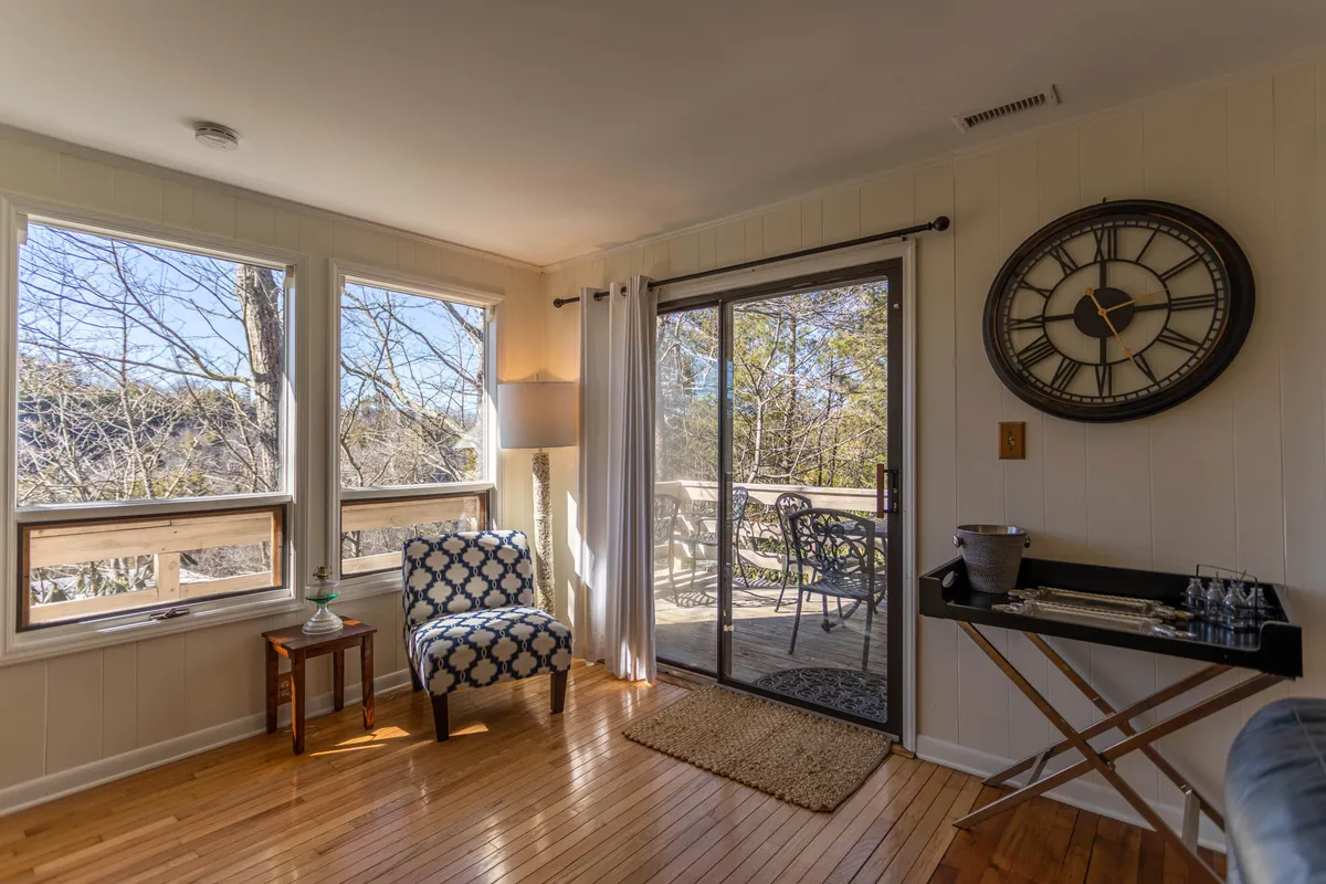 An interior living space with a blue and white patterned chair positioned near a large glass sliding door, allowing ample sunlight to fill the room. The open door visually connects the inside of the cottage to the outdoors, creating a seamless flow ideal for relaxing with your pet after outdoor adventures.